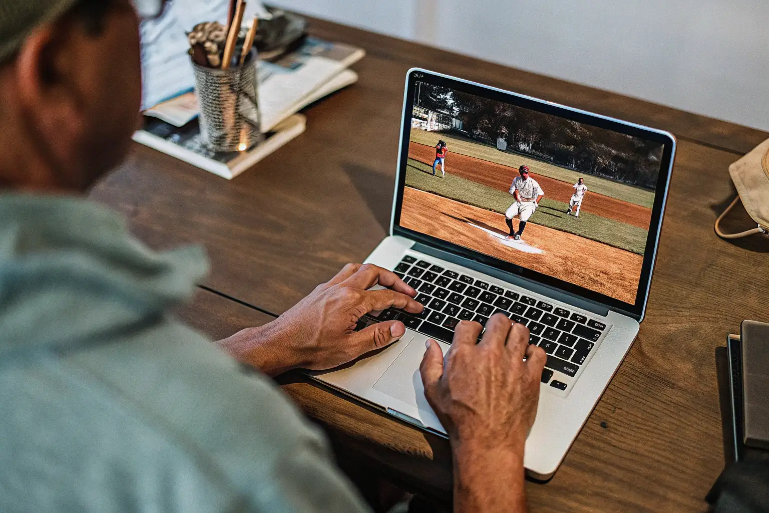 Sports journalist working at a laptop with college baseball game footage on the screen